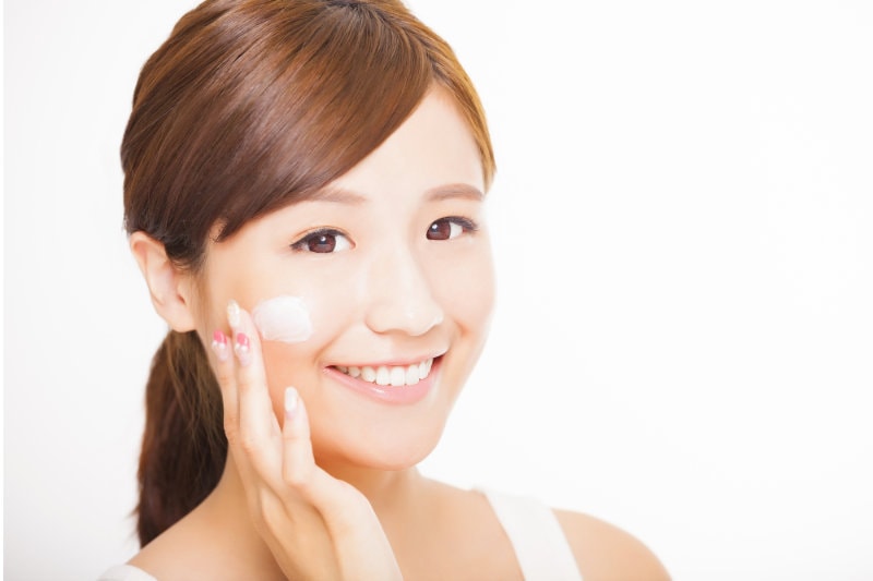 beautiful young woman applying cosmetic cream on her face
