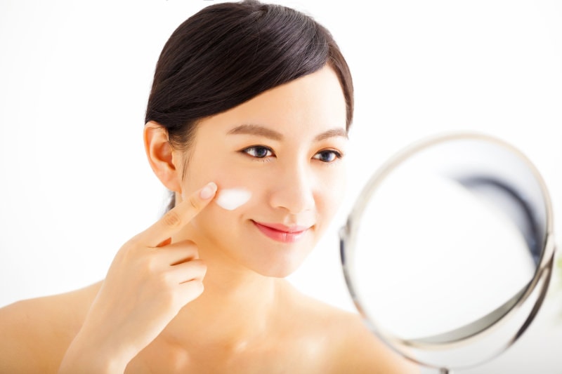 smiling woman applying cream lotion on face